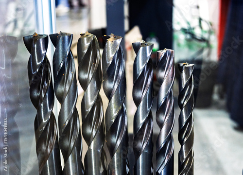 Row of sharp metal drill bits, showing twisted flutes and reflections. Essential drilling tools for industry, manufacturing, and workshops.