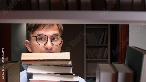 Student searching book in library, holding pile of books