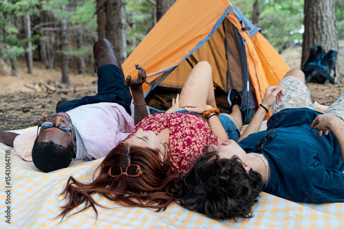 Diverse group of young friends relaxing and talking together on a blanket at a campsite