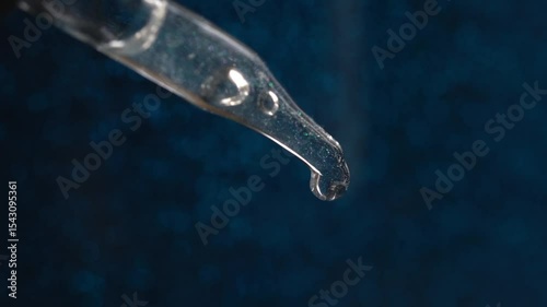 Glass pipette with facial serum on a light background. Essential oil close-up in a pipette. A skin care product with hyaluronic acid in a pipette.