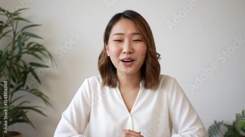 Young smiling Asian female on an online interview or making video call, sitting at desk and looking waving at camera, saying hello, woman takes a part in virtiual meeting. Job hunting. 