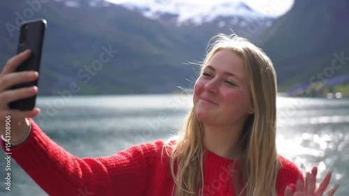 Beautiful woman taking selfie video using smartphone outdoors Girl sharing photograph on social media with mobile phone enjoying Norway vacation travel adventure 