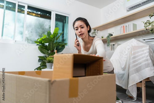 Moving process. Young woman packing boxes while on a phone call in a cozy home environment.