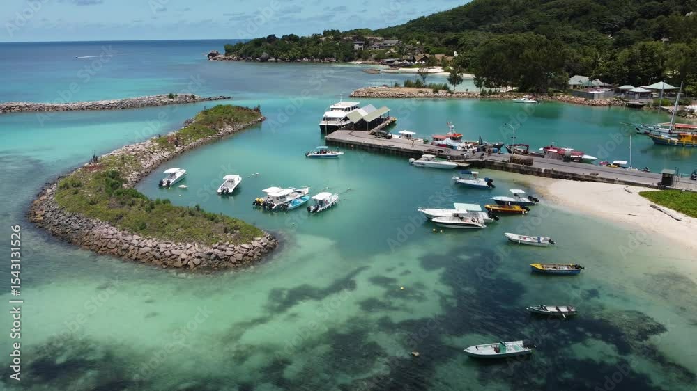 Drone shot of La Digue Island marina showing boats, clear waters, and lush green coastal landscape