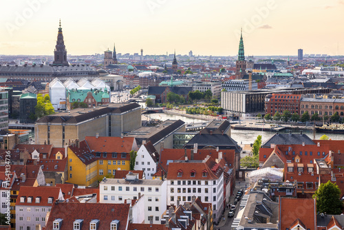 Panoramic view of Copenhagen taken from the top of the Church of Our Saviour, showing a mix of historical rooftops, modern buildings, and city landmarks under a warm evening sky.