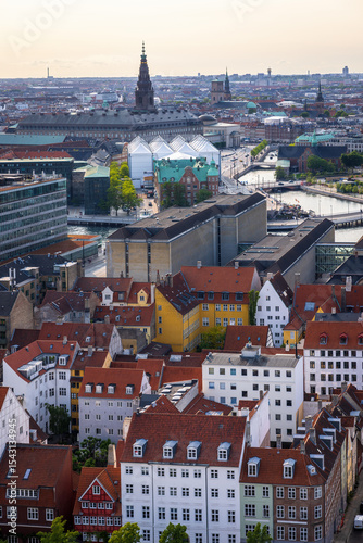 Panoramic view of Copenhagen taken from the top of the Church of Our Saviour, showing a mix of historical rooftops, modern buildings, and city landmarks under a warm evening sky.