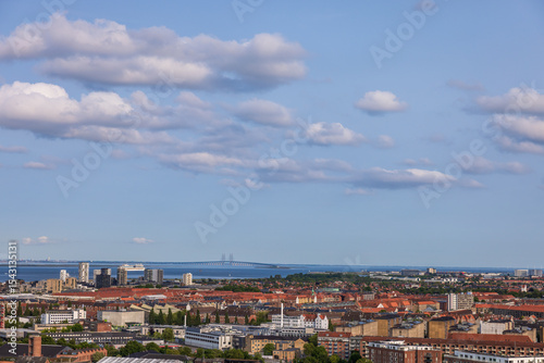 Panoramic view of Copenhagen taken from the top of the Church of Our Saviour, showing a mix of historical rooftops, modern buildings, and city landmarks under a warm evening sky.