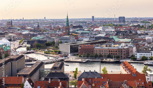 Panoramic view of Copenhagen taken from the top of the Church of Our Saviour, showing a mix of historical rooftops, modern buildings, and city landmarks under a warm evening sky.