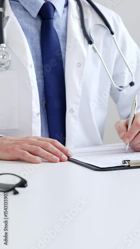 Male doctor writing a prescription and filling out medical records on a clipboard in an office setting, showcasing the essential aspects of healthcare and patient care. Medicine and health care