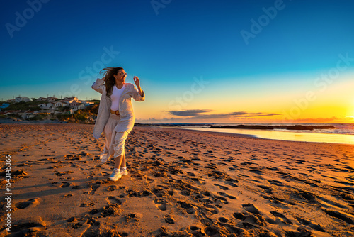 Beautiful middle-aged woman enjoying walk on sandy beach on sunset on windy spring day. Front view. Monte Clerigo beach on Algarve coast in Portugal