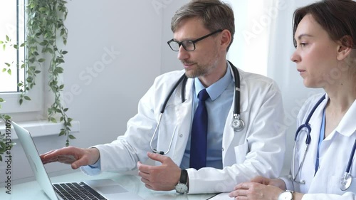 Two doctors are examining medical records on a laptop, engaging in a focused discussion about patient data within a hospital or clinical setting. Medicine and health care concept.