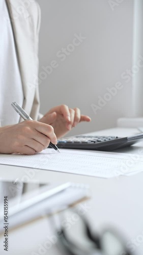 Businesswoman is calculating annual tax using calculator and taking notes in the office, managing domestic budget and checking financial documents. Audit and taxes in business