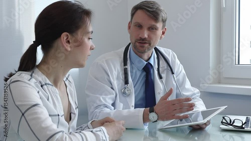 Doctor showing information on a digital tablet to a patient during a medical consultation in a bright office, discussing diagnosis and treatment options. Medicine and health care
