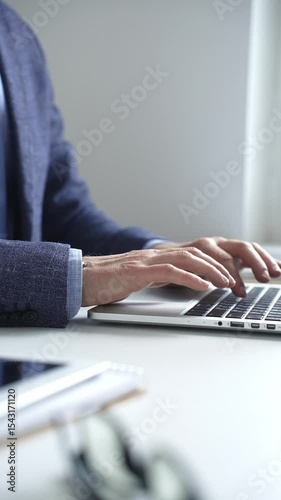Close up of businessman's hands typing on laptop keyboard, working diligently in a modern office setting, wearing a suit and watch. Business people concept