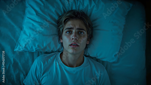 Young man awake in bed with concern