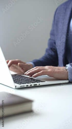 Close up of businessman's hands typing on laptop keyboard, working diligently in a modern office setting, wearing a suit and watch. Business people concept