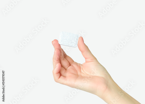 Hand holding a small white dishwasher tab isolated on white background 