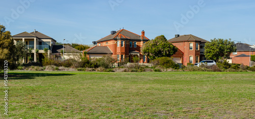 An open grassy field in a suburban park in Australia under a clear blue sky with a row of residential houses in the background.Concept of community living, Australian parkland, and local outdoor space