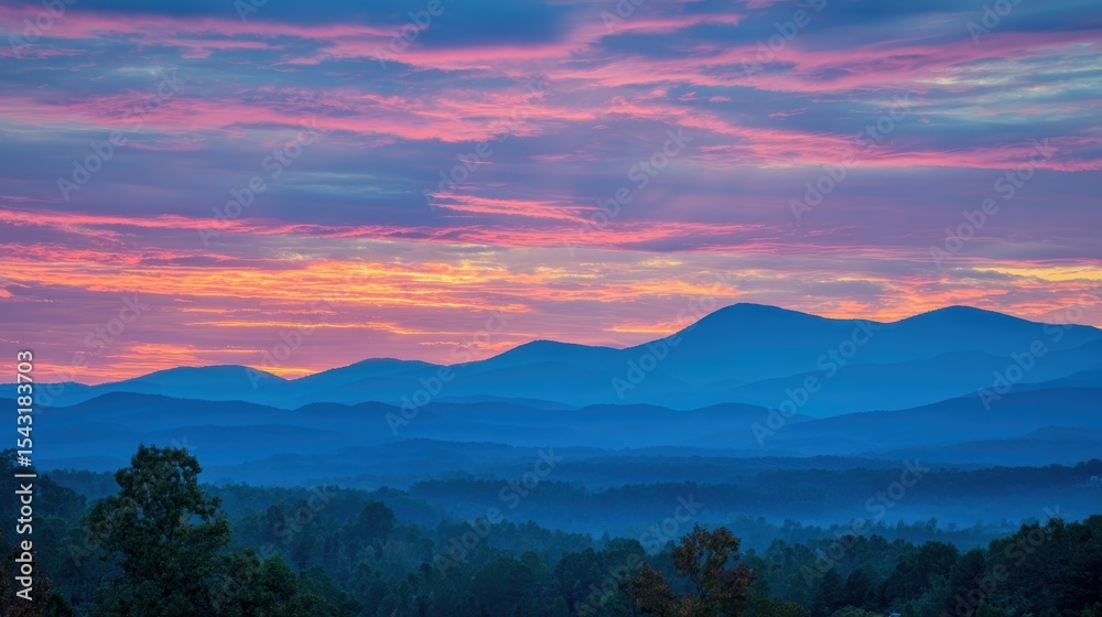 Fototapeta premium Colorful sunrise over blue mountain ranges with vibrant clouds and misty forests in the foreground