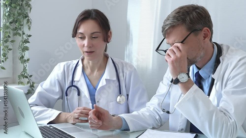 Two doctors are examining medical records on a laptop, engaging in a focused discussion about patient data within a hospital or clinical setting. Medicine and health care concept.
