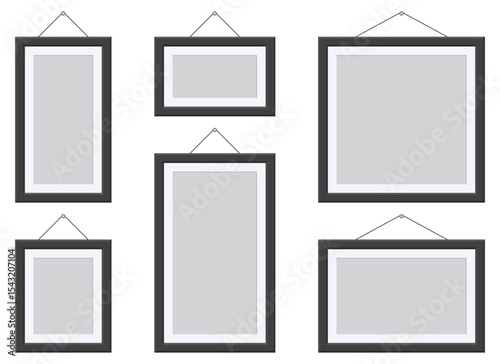 Several empty picture frames of different sizes and orientations hang against a plain background. Each frame features a dark border and a string for hanging.