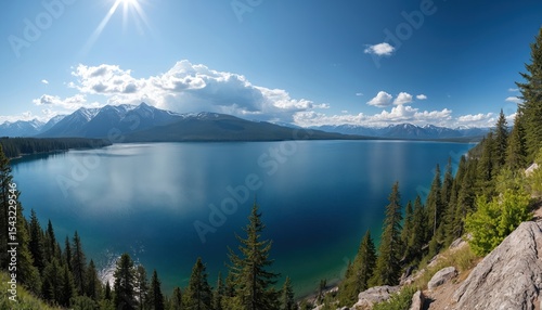 Panoramic view of Flathead Lake in Montana. Clear blue water reflects sky with mountains covered snow. Rich evergreen forest meets shoreline. Perfect summer travel destination, eco tourism spot.