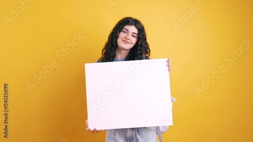 Young student presenting white blank board on yellow background