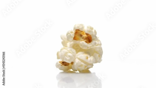 A piece of popcorn with a white exterior and exposed yellow kernel sits on a reflective white surface