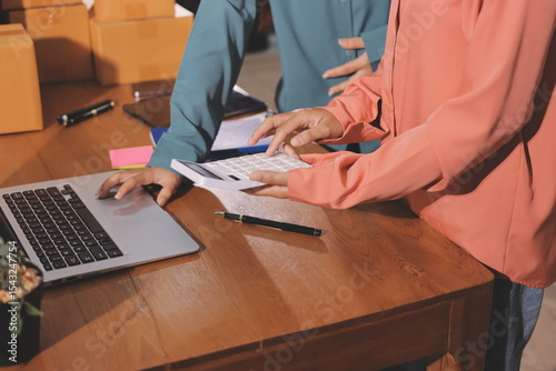 Startup SME small business entrepreneur of freelance Asian woman wearing apron using laptop and box to receive and review orders online to prepare to pack sell to customers, online sme business ideas.