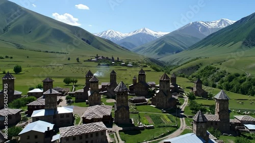 Verdant valley village with stone towers set against snowcapped peaks under a clear blue sky