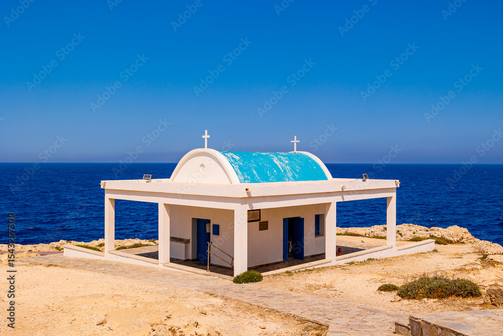 Fototapeta premium Seaside Chapel with Blue Dome and Ocean View in Cyprus,small white chapel with a light blue dome and crosses, perched on a rocky coastline in Cyprus with the Mediterranean ,summer travel , hot summer 