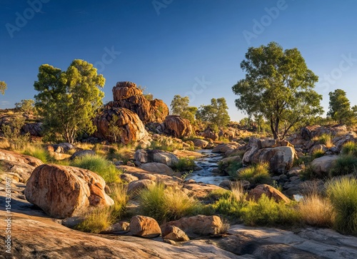 A beautiful landscape of the late afternoon in Australia's outback, with a clear blue sky, boulders and rocks on the ground surrounded by green vegetation around a small river, and a few eucalyptus 