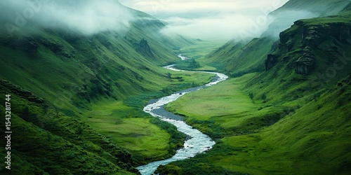 A winding river flows through a lush green valley surrounded by misty, rugged mountains under a cloudy sky. photo