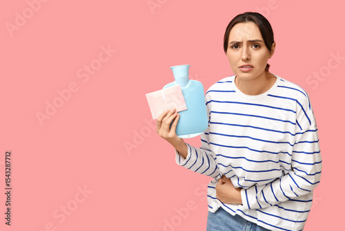 Young woman with hot water bottle and pad suffering from menstrual cramps on pink background