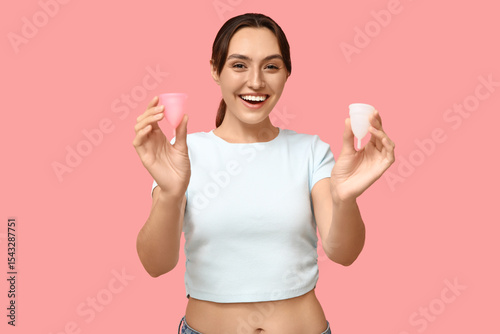 Beautiful young woman with menstrual cups on pink background