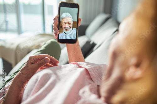 Senior woman video calling her partner on smartphone from home couch