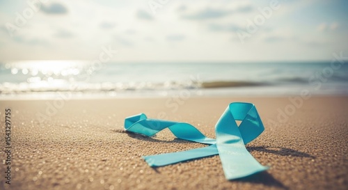A Turquoise Awareness Ribbon Lies on the Sandy Beach with Ocean and Horizon Background