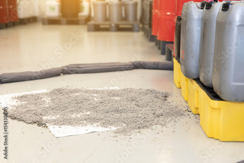 Spill containment barrier surrounding large oil spill with chemical storage drums in warehouse