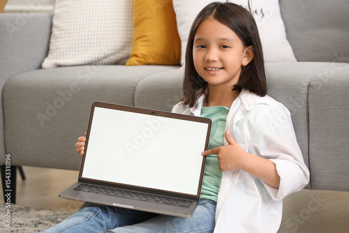 Little Asian girl with blank laptop at home