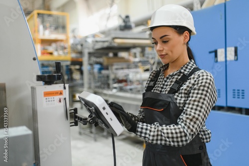 Female factory worker operating machinery using digital tablet in modern industrial plant