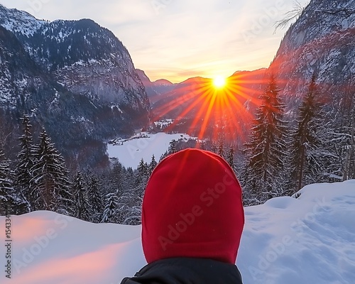 A person watches a winter sunset over snowy mountains and trees