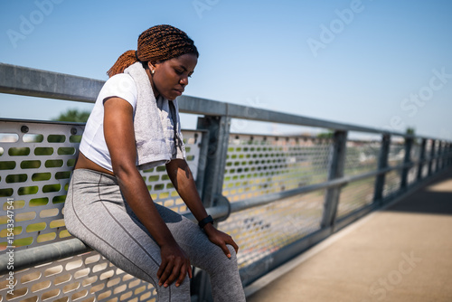 Portrait of young sporty African-American woman in sportswear looking tired and disappointed while sitting after difficult exercising outdoor on a sunny day.