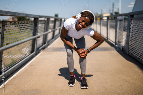 Worried young African-American woman in sportswear having sport injury during exercising outdoor. She is having pain in her knee.