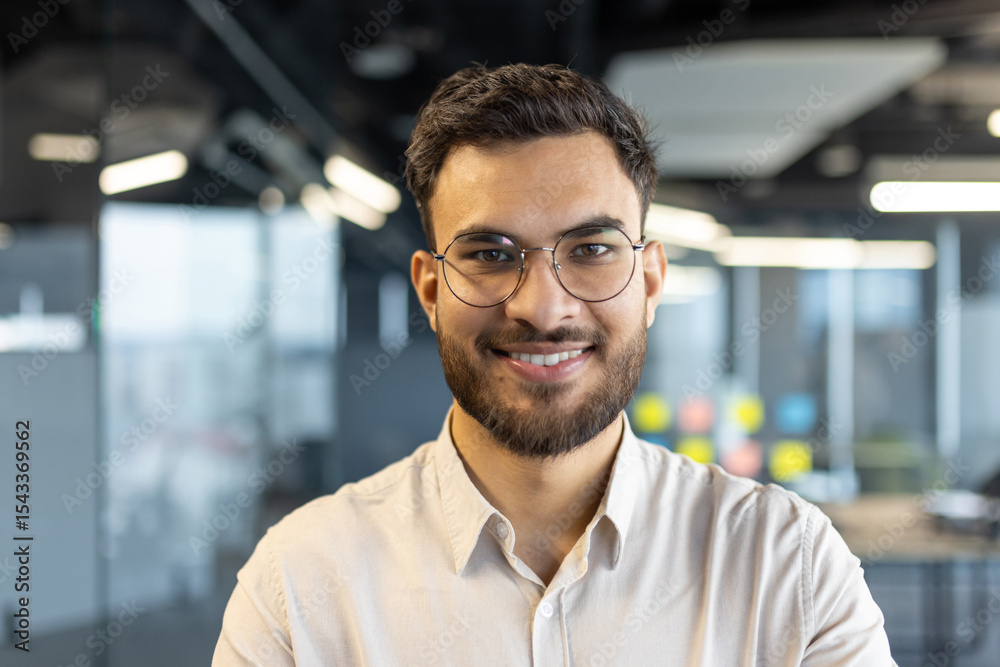 Obraz premium A smiling businessman wearing glasses poses in a modern office setting, showcasing a confident and professional image.