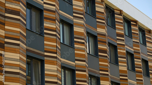 Modern building facade with distinctive striped pattern, blend of natural aesthetics and contemporary design. Dark grey sections with windows. Warm, earthy tones. Innovative architectural cladding.