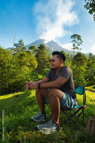 Man Relaxing Outdoors With Scenic Merapi Mountain and Lush Greenery in the Background