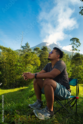 Man Relaxing Outdoors With Scenic Merapi Mountain and Lush Greenery in the Background