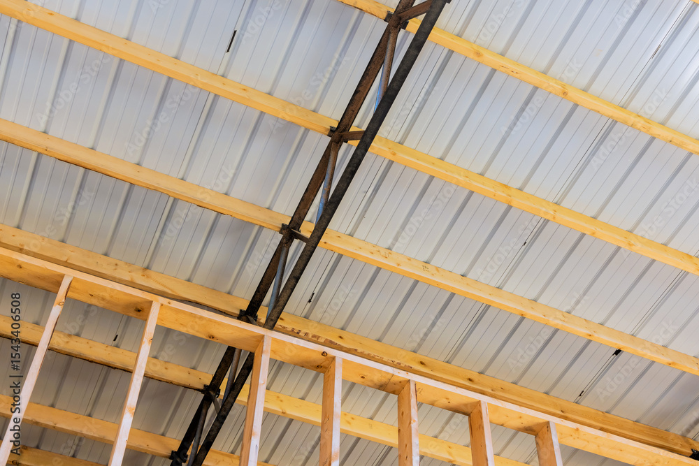 Fototapeta premium Wooden beams metal supports are visible during construction of building with sheet metal roof.