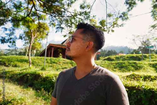 Man Wearing Glasses in a Serene Countryside Landscape with Lush Greenery