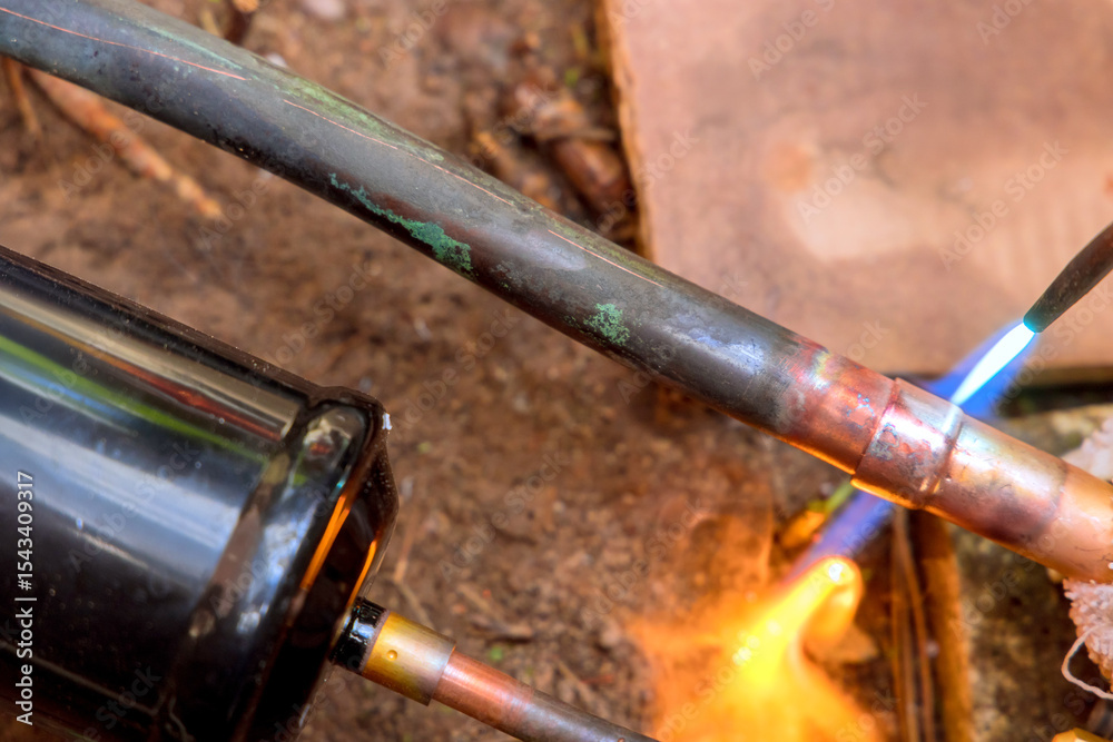 Naklejka premium Flame from torch heats copper pipe joints, preparing for soldering in workshop filled with tools materials.